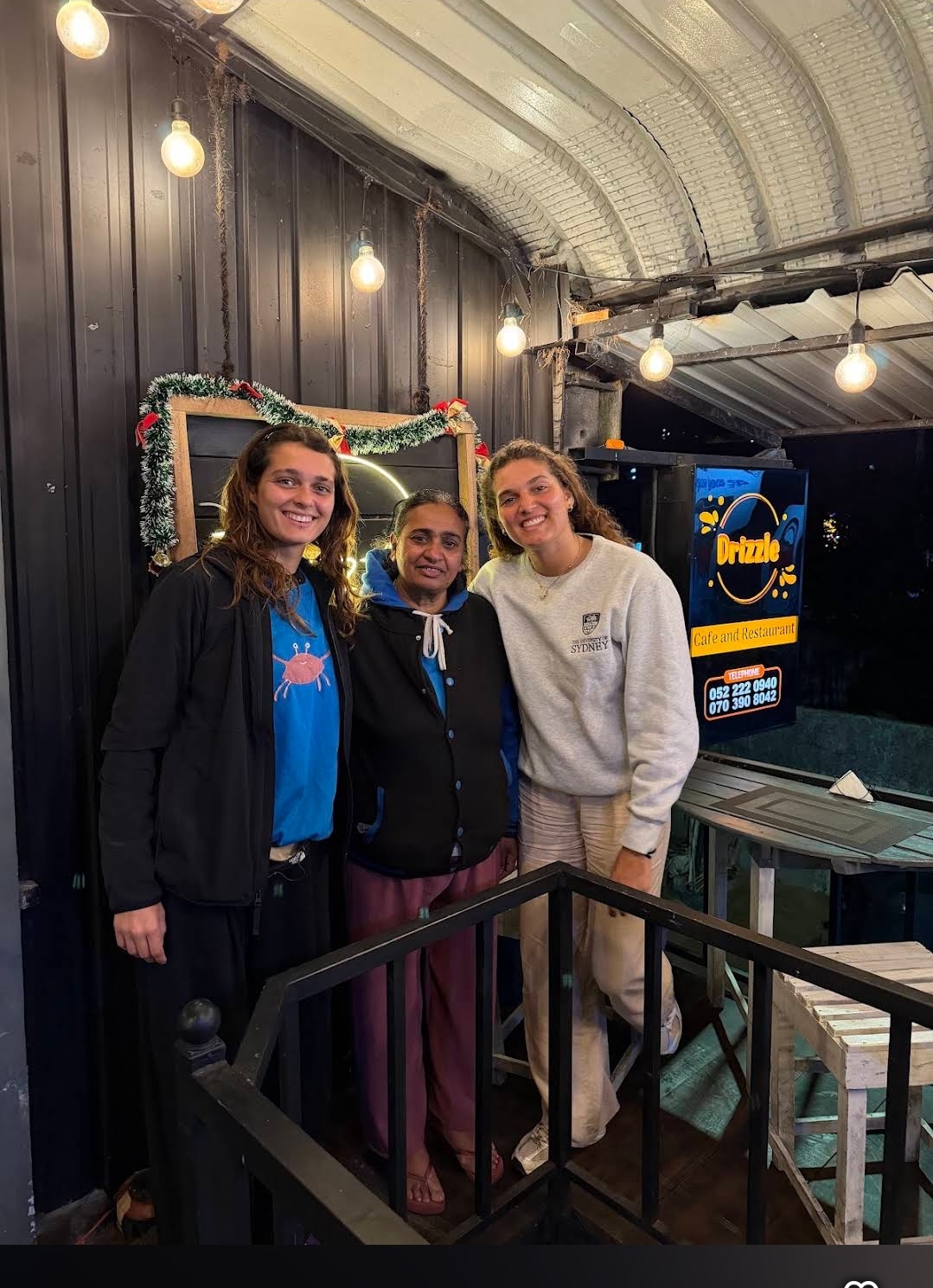 Guests posing beside the Drizzle Café sign on the fairy-lit balcony